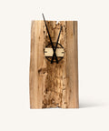 Minimalist wall clock with brass or gold-colored hands mounted on a dark, distressed wooden board, displayed within a wooden frame or shelf.