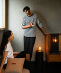 Interior room scene with vintage Edison bulb lamps, showing two people in a casual setting - one seated on a tan couch with a decorative pillow, wearing a white t-shirt, and another standing wearing a black and white striped shirt, with warm ambient lighting creating a cozy atmosphere.