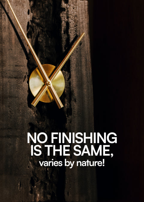 Minimalist wall clock with brass or gold-colored hands mounted on a dark, distressed wooden board, displayed within a wooden frame or shelf.